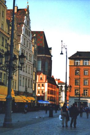 Vi befinner oss på Rynek (”Torget”). Här ser vi den västra sidan av torget, kallad ”Ullmarknaden”. Sydsidan kallas ”Fiskmarknaden” och norrsidan ”Sötsaksmarknaden”. I bakgrunden skymtar Elisabetkyrkan.